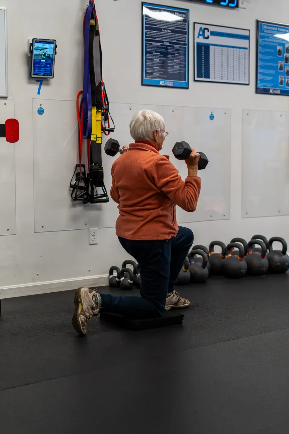 Member doing a kneeling dumbbell press in front of a rack of kettlebells