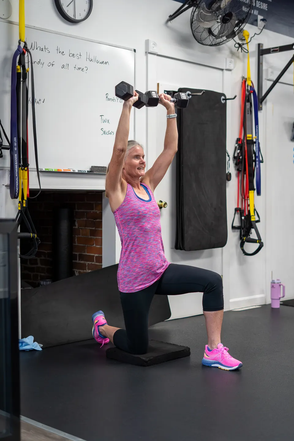 Member pressing a dumbbell overhead from a kneeling position