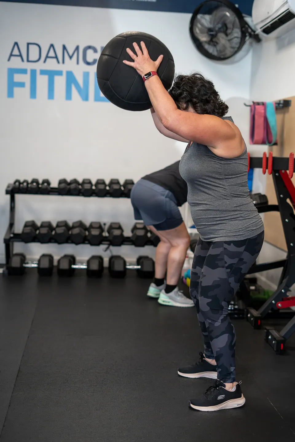 Brand photography for Adam Clark Fitness in Brewer, Maine: a member lifting a slam ball under the gym's logo