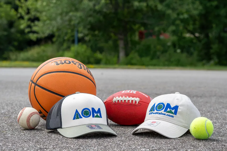AllOutMaine hats with a basketball, football, baseball and tennis ball on a court