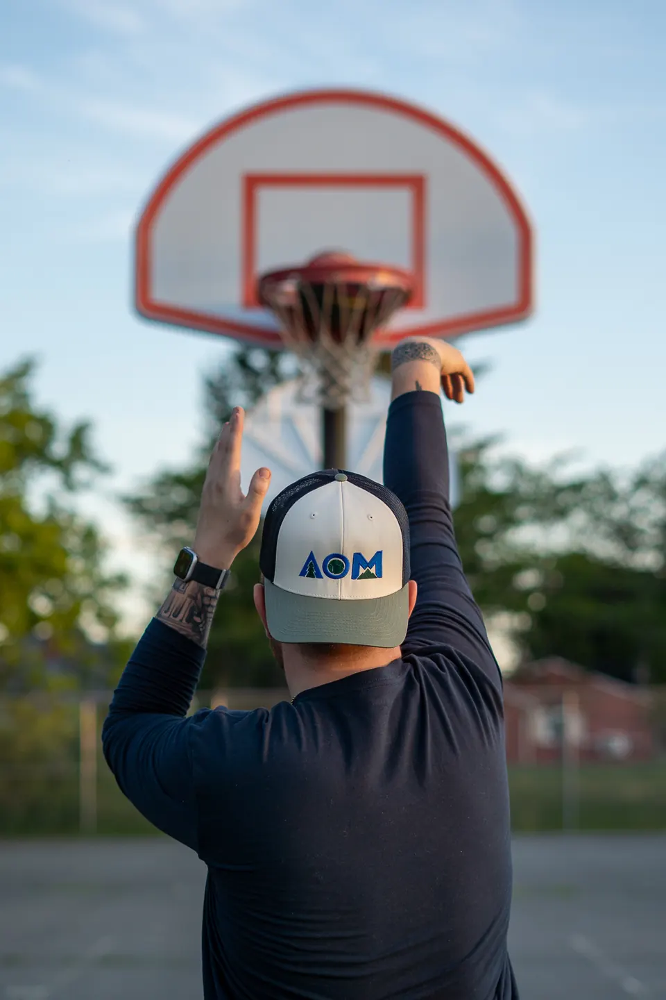Basketball player rising for a shot at an outdoor court at sunset, wearing an AllOutMaine hat