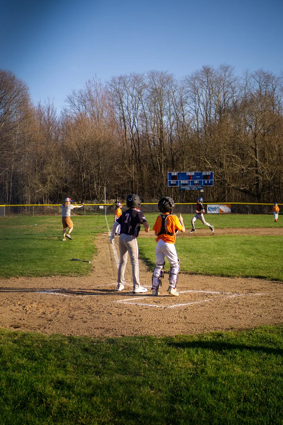Youth baseball game in progress under bare spring trees