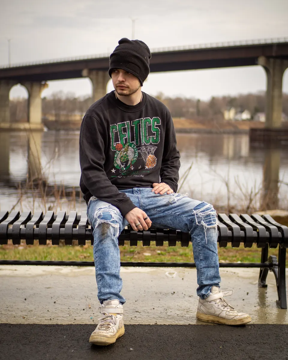 Young man sitting on a bench under a river bridge