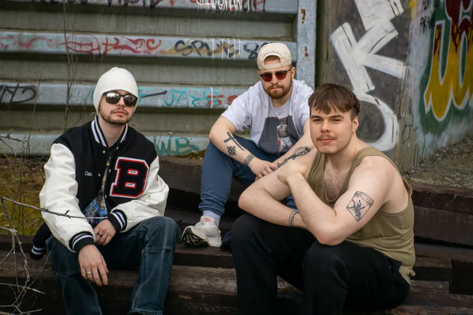Three friends in streetwear sitting under a graffiti bridge