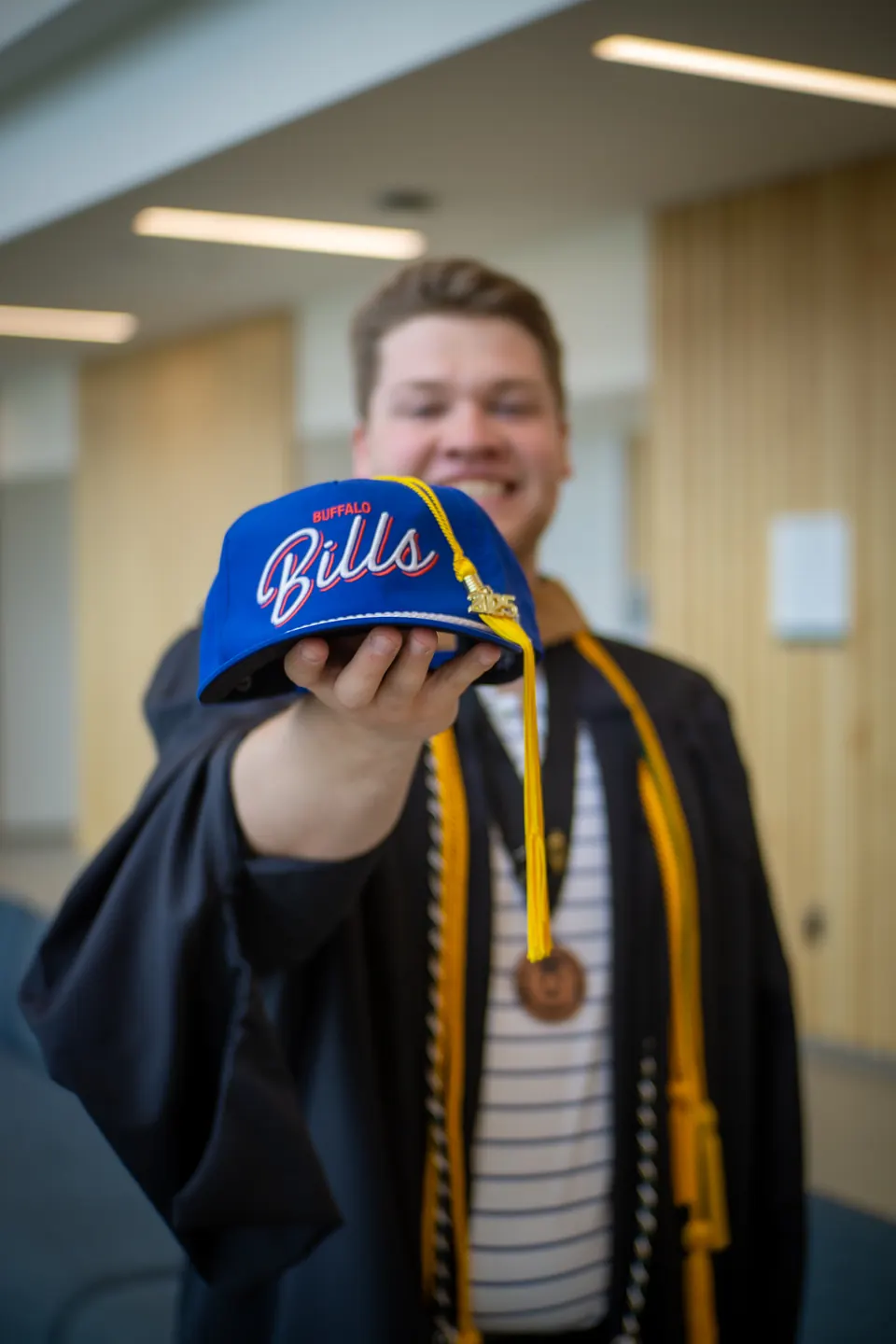 College graduate holding up a Bills cap in a campus building
