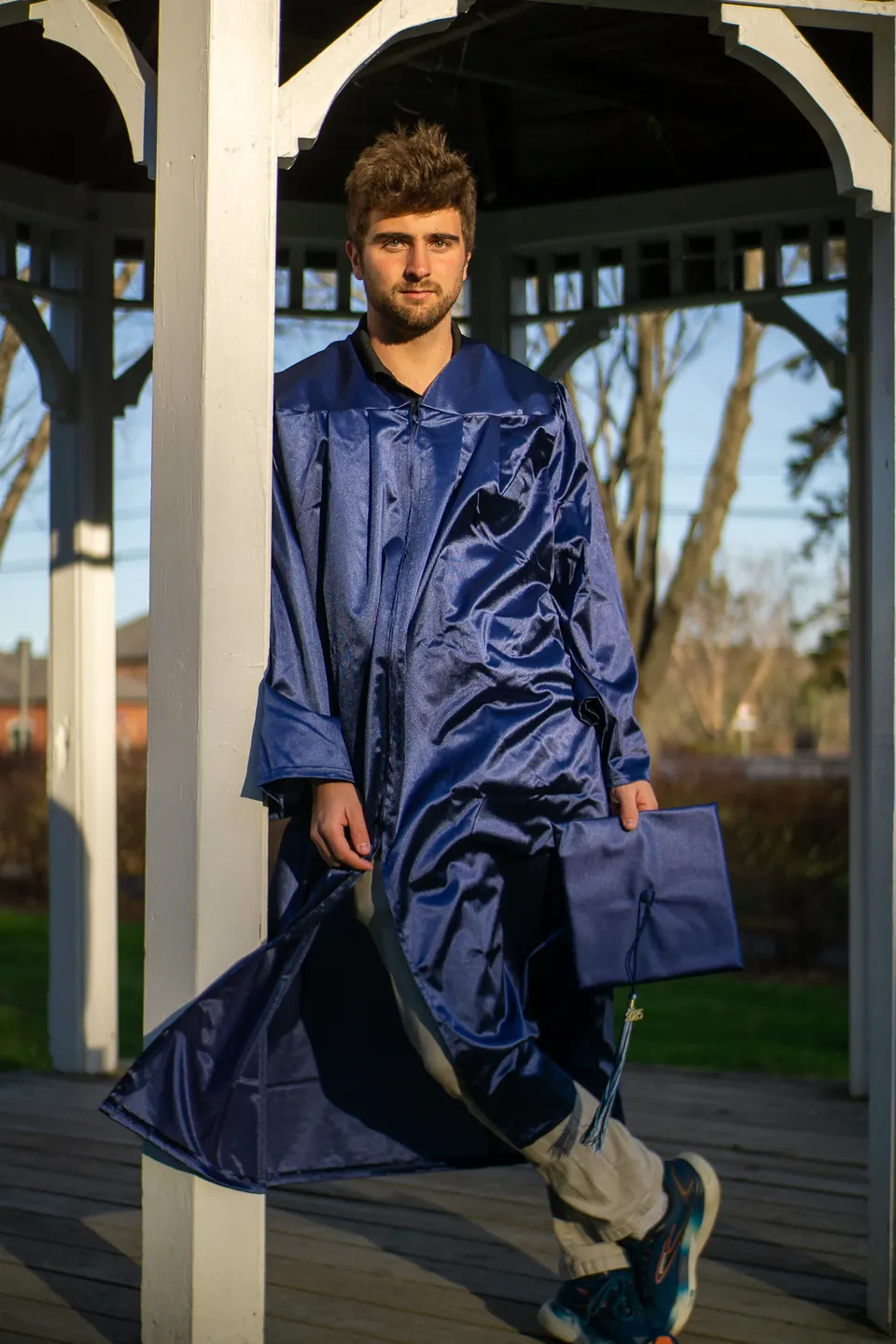 Graduate in a blue gown walking out of a white gazebo