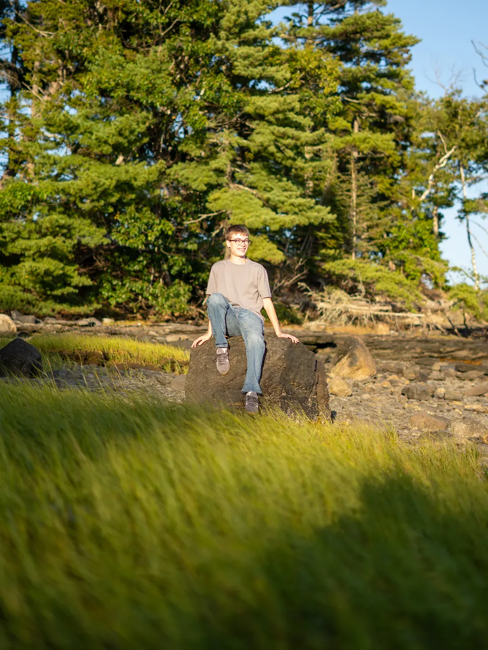 Senior standing in tall grass in front of a stand of pines