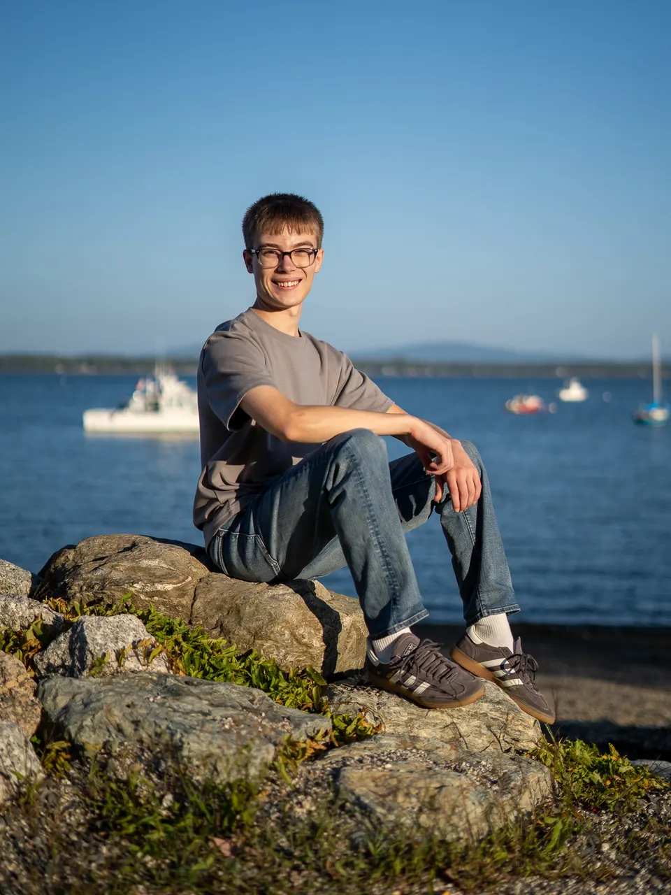 Senior sitting on a rock above a harbor with moored boats