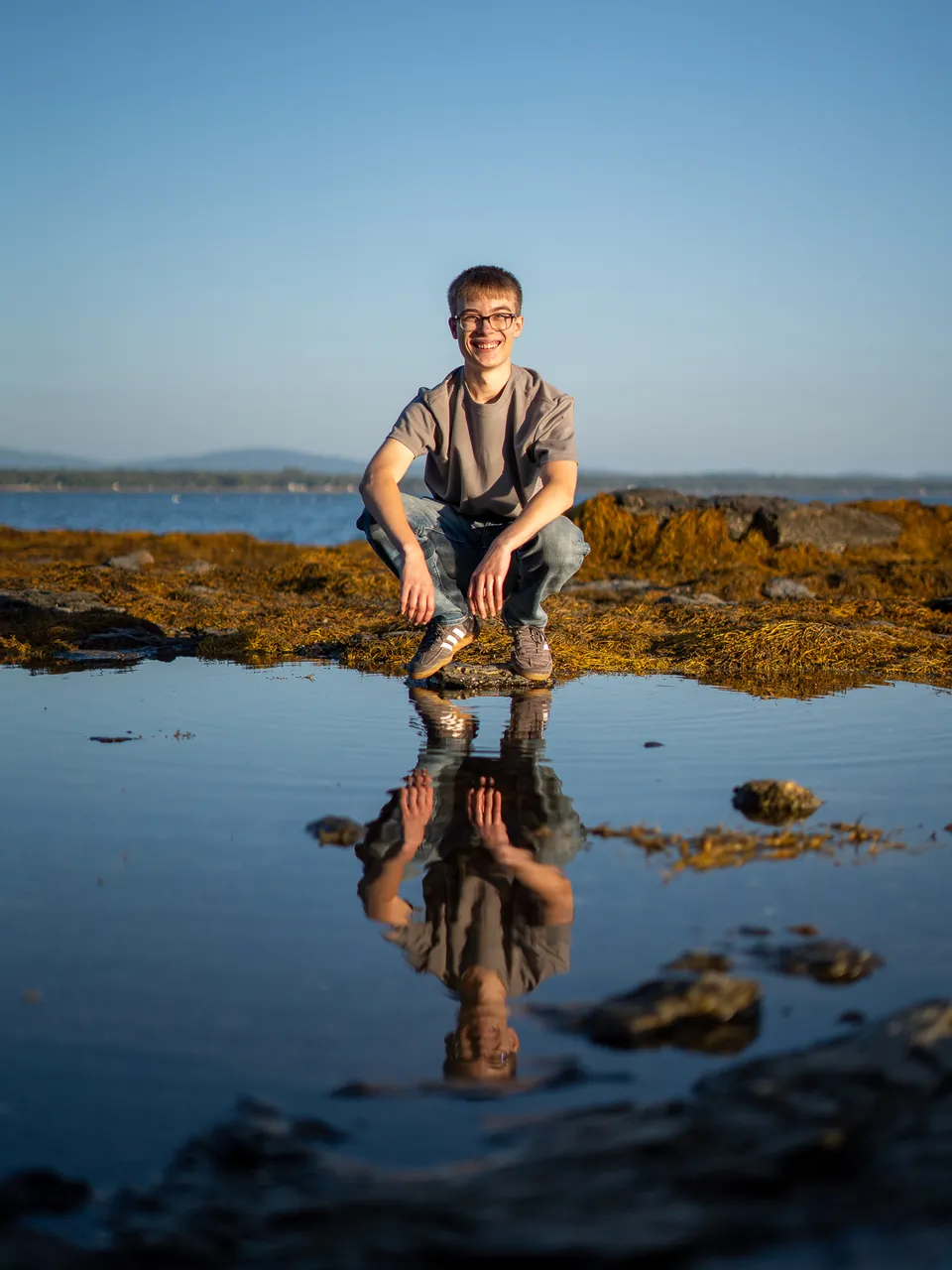 Senior portrait on the Maine coast, reflected in a tide pool at golden hour