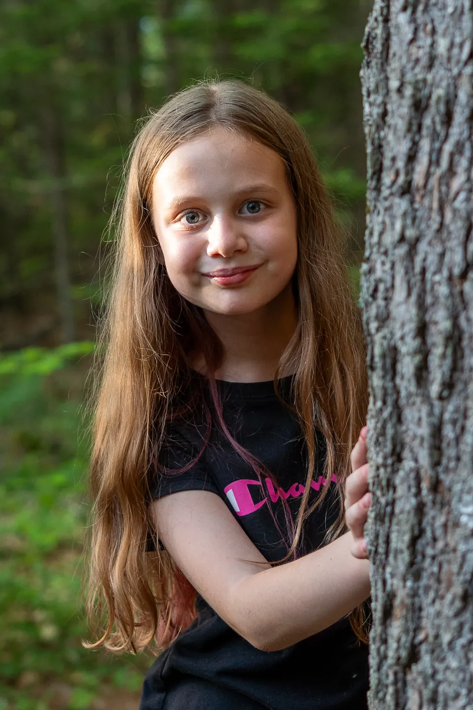 Girl peeking out from behind a tree trunk in the forest