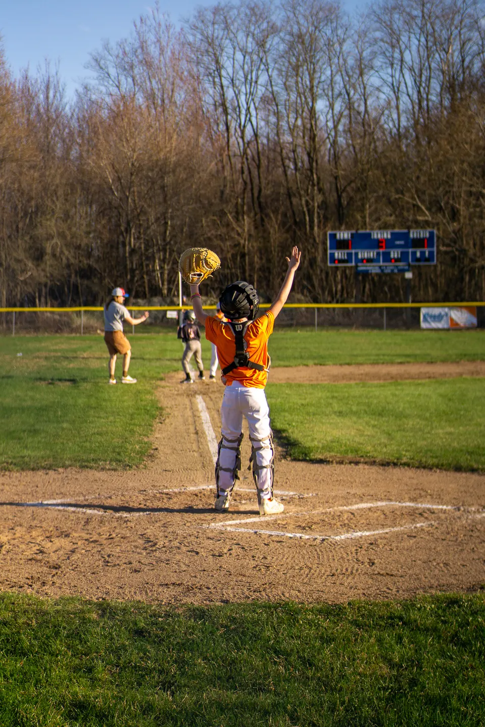 Youth baseball pitcher mid-windup on a spring evening