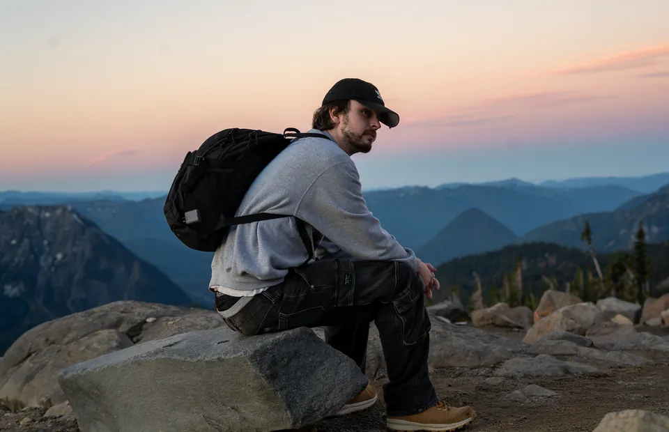 Hiker resting on a ridge above layered blue mountains at sunset