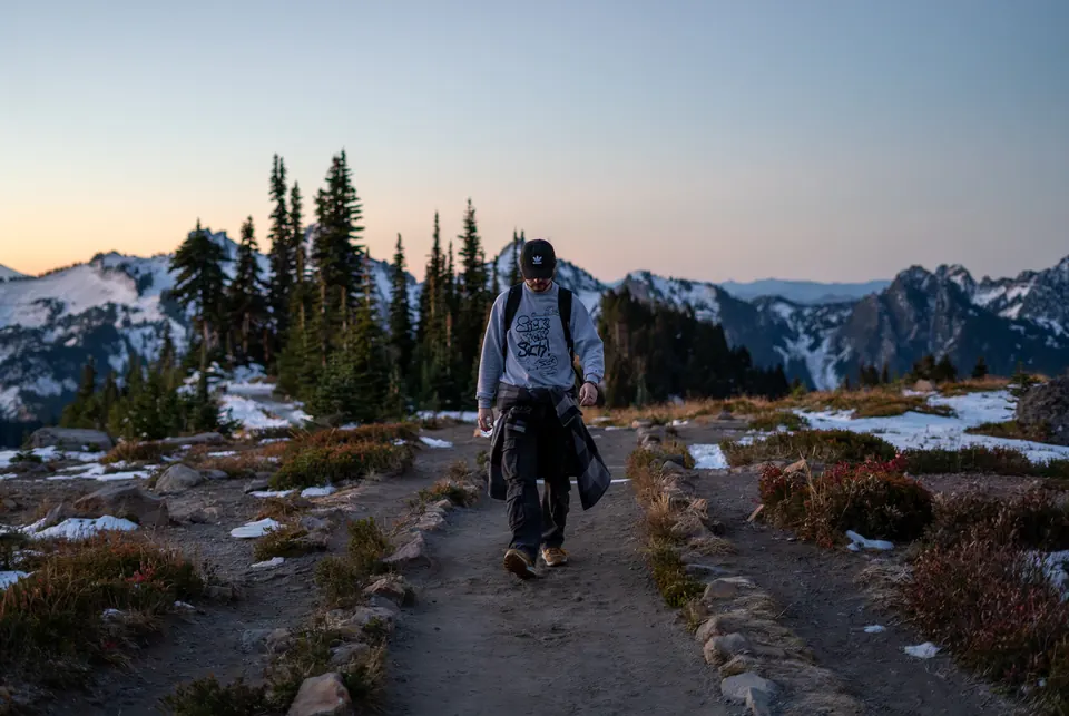 Hiker on a trail through snow-dusted alpine meadows