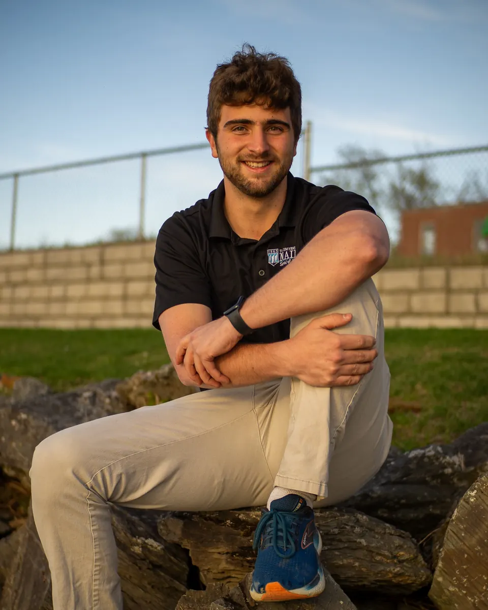 Senior sitting on a stone wall by a ball field