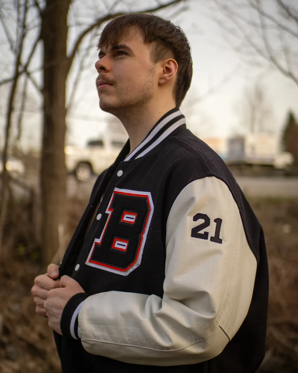 Senior in a varsity jacket looking off at golden hour